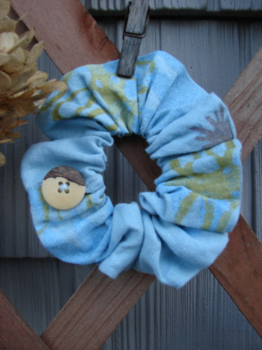 2000 PMU Linen Hemp Button Hair Scrunchie Abstract Sun Water Small, featuring a ruffled fabric with a button detail, displayed on a wooden bar, showcasing its sustainable and vintage-inspired design.