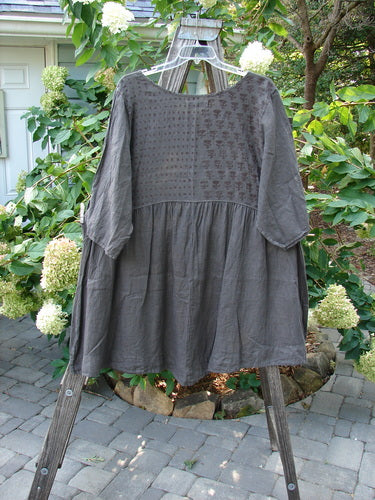 Barclay Linen Two Pocket Dolly Dress Butterfly Wood Size 2 displayed on a clothes rack, featuring flouncy lower skirt, dropped empire waist, wide hem sweep, dual lower pockets, and butterfly-themed paint on upper bodice.