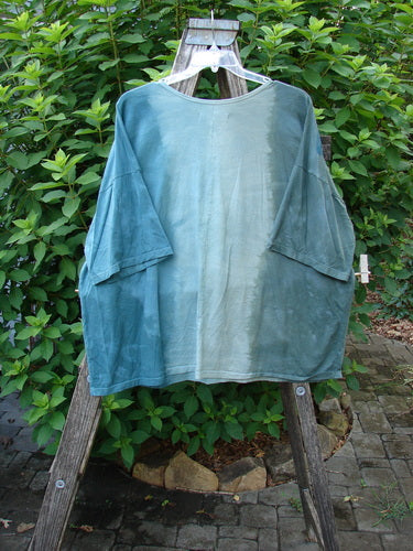 Barclay Center Seam Wide Line Tee Floral Path Mottled Turq OSFA displayed outdoors, highlighting its boxy shape, vertical center seam, and drop shoulders on a wooden stand amidst greenery.