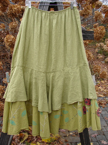 Barclay Linen Two Tier Ruffle Skirt Ladybug Yellow Olive Size 2 displayed on a rack, featuring a floral design, thinner elastic waistline, and a wide, double A-lined fall with a large lower ruffle.