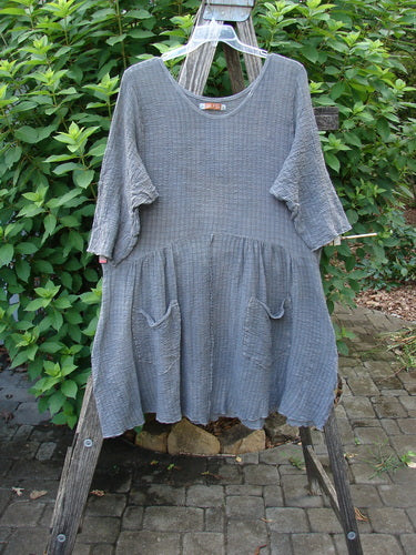 Barclay Crinkle Gauze Two Pocket Dolly Dress Mottled Slate Size 1 displayed on a swinger, showcasing its flouncy dual-pocketed lower skirt, three-quarter sleeves, and distinctive downward curved empire waist seam.