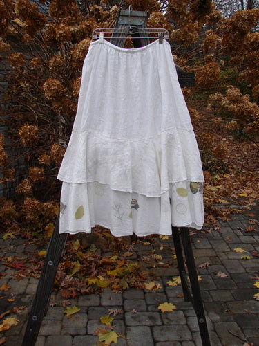 Barclay Linen Two Tier Ruffle Skirt Tiny Birdie White Size 2 displayed on a rack, featuring a thinner elastic waistline, wide double A-line fall, and tiered ruffles for a layered look.