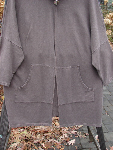 Barclay Hemp Cotton Open Front Hooded Cloak Twig Stone OSFA hanging on a rack, showcasing its cozy hood, kangaroo pockets, dolman sleeves, and generous, flowing design.