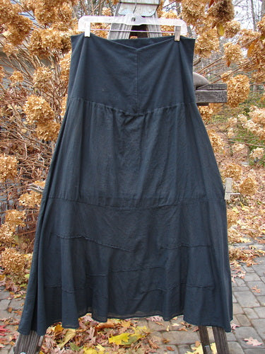 Barclay Batiste Fold Over Wave Layer Skirt Unpainted Black Size 2 on a clothes rack, showcasing its full paneled waistline, varying hemline with horizontal pinched waves, and large lower sweep.