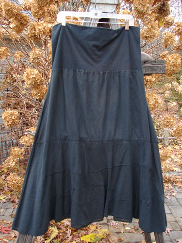 Barclay Batiste Fold Over Wave Layer Skirt Unpainted Black Size 2 displayed on a clothes rack, showcasing its unique paneled waistline and varying hemline with horizontal pinched waves.