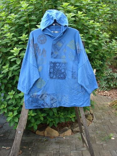 Barclay Dolman Roo Pocket Hoodie Mixed Theme Skylark OSFA features a cordless hood and dolman shoulders, displayed on a wooden stand, exemplifying Bluefishfinder.com's unique, expressive vintage outerwear style.