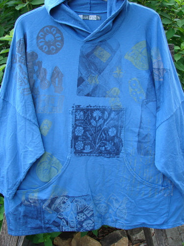 Barclay Dolman Roo Pocket Hoodie Mixed Theme Skylark OSFA features a circular flower patch on a blue shirt, highlighting cozy dolman sleeves and unique painted drop pockets, reflecting BlueFishFinder’s vintage-inspired creativity.