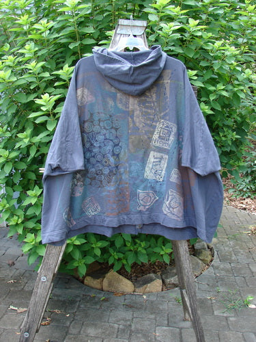 Barclay Hooded Postcard Zipper Jacket Vest Rear Home Raven OSFA displayed outdoors on a swing, highlighting its generous hood, full zipper, dolman shoulders, and varying hemline, emphasizing its cozy and unique design.