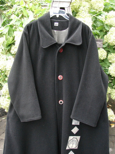 1999 Patched Woven Wool Overcoat in jet black, size 2, with a broad rounded collar, three front buttons, and loose sleeves. The heavy wool drapes in a clean, dark silhouette, while a row of pale patches adds contrast near the lower front.