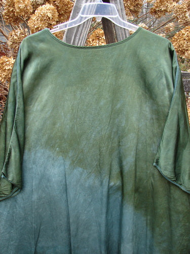 Barclay Viscose Hi Low Tunic Wildflower Forest Sun Size 2 displayed on a wooden fence, showcasing its rounded neckline, varying hem, and three-quarter dolman sleeves with exterior stitching.