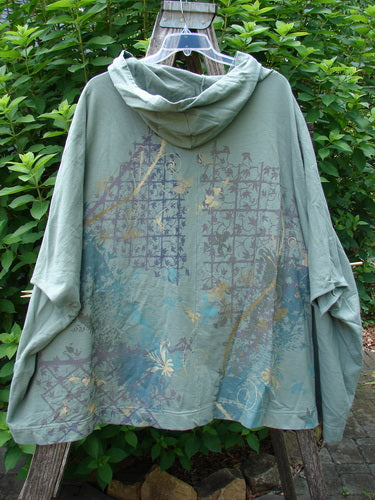 Barclay Hooded Postcard Zipper Jacket Vest in Sage, featuring a generous hood, full zipper, dolman shoulders, and a unique rear garden trellis design, displayed on an outdoor swinger.