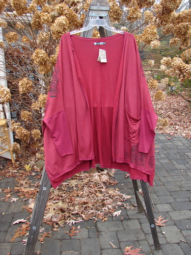 Barclay NWT Rayon Lycra Celebration Cardigan Spirograph Rouge OSFA hanging on a rack, showcasing its open front, flutter hem, and dolman three-quarter length sleeves with vented sides.