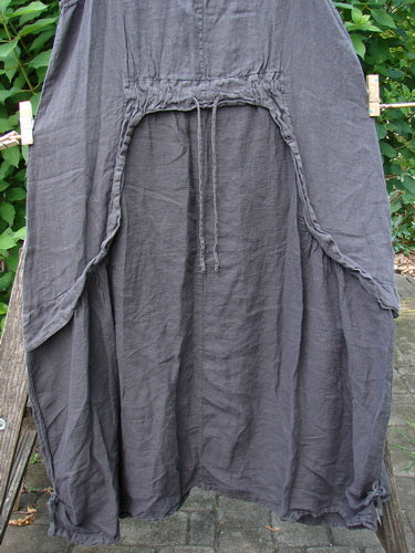 Barclay NWT Linen Explorer Jumper Contour Garden Black Sand Size 0 displayed outdoors, showcasing its full A-line shape, scoop neckline, and unique exterior upper pocket, hung on a clothesline.