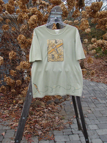 2001 Short Sleeved Tee Glider Plane Kelp Size 1 displayed on a stand, featuring drop shoulders, wide short sleeves, a slightly thinner flattened neckline, and a glider plane design on the front.