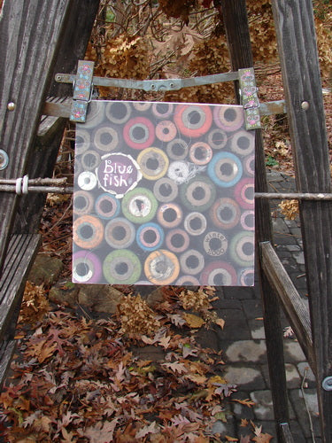 2000 Winter Catalog Rhythm and Texture One Size, featuring vibrant art and poetry, placed on a ladder surrounded by outdoor autumn elements, offering a nostalgic dive into vintage Blue Fish designs.