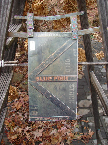 A wooden sign on a ladder, showcasing the 2000 Transitions Catalog An In Between Place One Size, featuring color charts, line drawings, vintage images, and poetry, from the BlueFishFinder's vintage collection.