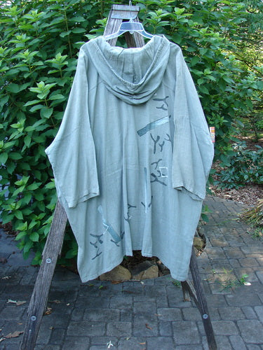 1997 Linen Seaspray Jacket Bamboo Lagoon Size 3 displayed on a clothes rack, showcasing its oversized floppy drawcord hood, dolman sleeves, generous shirttail hemline, and bamboo theme paint with front metal buttons.