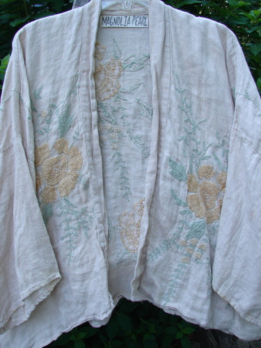 Magnolia Pearl Linen Embroidered Claudio Kimono Lilac Water OSFA features pastel floral embroidery on medium weight linen, with an open front, dolman shoulders, and wide three-quarter sleeves, embodying vintage-inspired elegance.