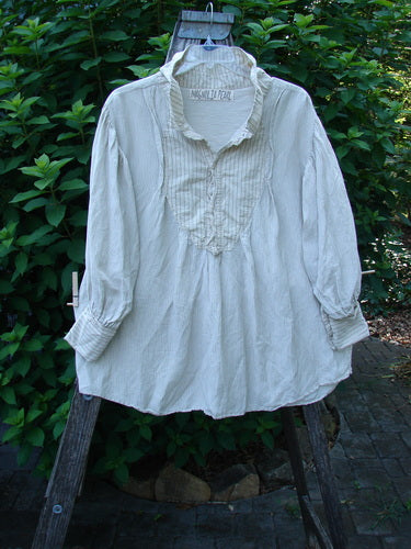 Magnolia Pearl Linen Crop Artist's Pocket Pullover features a lightweight, cream long-sleeve blouse with a ruffled placket, stand-up collar, and gathered cuffs, displayed outdoors on a wooden ladder.