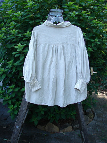 Magnolia Pearl Linen Crop Artist's Pocket Pullover Brown Army OSFA displayed on a wooden ladder, showcasing its Henley button front, stand-up collar, laced crinkle bib, and distinctive pinstripe pattern against a lush greenery backdrop.