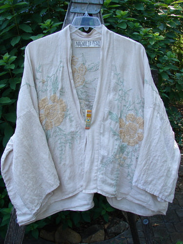 The Magnolia Pearl Linen Embroidered Claudio Kimono Lilac Water OSFA features intricate pastel floral embroidery, wide three-quarter sleeves, and a stand-up collar, embodying vintage elegance from Bluefishfinder.com.