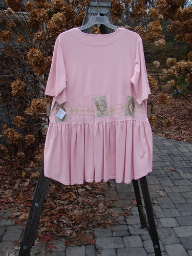 1999 NWT Garden Herb Dress Rooster Peony Size 1 hanging on a rack, featuring four-paneled pockets, a ceramic top button, drop waistline, full skirt with folds, and rooster-themed design.