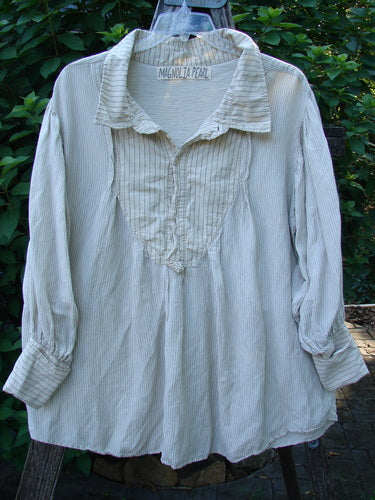 Magnolia Pearl Linen Crop Artist's Pocket Pullover features a cream-colored, lightweight blouse with a pintucked bib, button cuffs, and a small collar, hanging elegantly on a wooden ladder.
