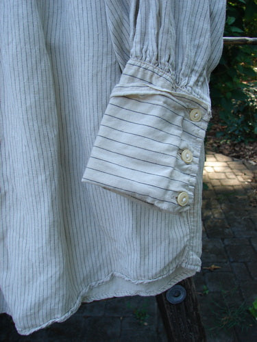 Magnolia Pearl Linen Crop Artist's Pocket Pullover: Close-up of the sleeve, highlighting fine pin-stripes and three-button cuff, draped outdoors, showcasing meticulous craftsmanship and vintage-inspired style.
