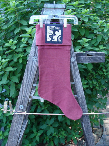 1995 Reprocessed Holiday Stocking Festive Hollyberry OSFA featuring striking blue fish holiday paint and a bright signature patch, displayed hanging on a wooden ladder, embodying vintage charm and festive cheer.