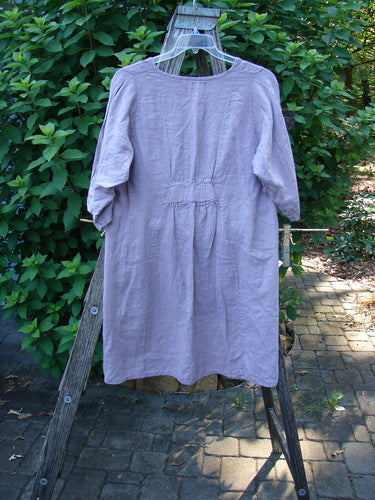 Barclay NWT Linen Posey Tunic Dress in Orchid Field Sea Fog Size 0 features an oval neckline, flowy figure-eight shape, nearly three-quarter sleeves, and two front pockets on a wooden stand.