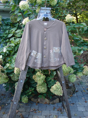 1999 Coffee Top Fancy Pot Riverbed Size 1 displayed on a wooden ladder, showcasing its sweeping rounded hemline and button closures, capturing the vintage charm of Blue Fish Clothing's Spring Collection.