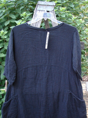 Barclay NWT Gauze Seaside Tunic Dress Unpainted Black Size 0 displayed on a hanger, highlighting its varying hemline, gently scooped flutter neckline, drop shoulders, and wide short sleeves against an outdoor backdrop.