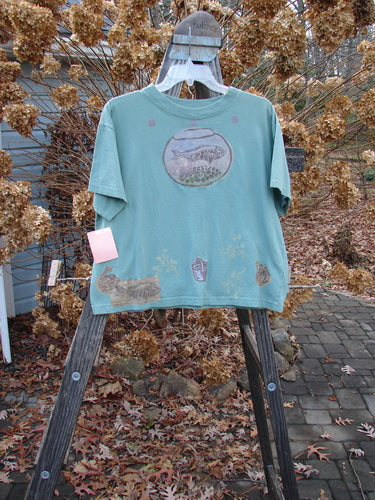 1994 NWT Short Sleeved Tee Fish Bowl Seagrass Size 3, featuring a fish bowl graphic, thick ribbed neckline, and bottom flair, displayed hanging on a wooden ladder.