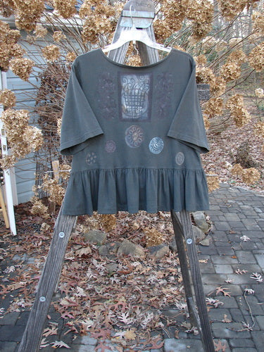 1992 Holiday Short Sleeved Peplum Top Black Sand Size 1: A grey shirt with a pattern on it, on a wooden rack.