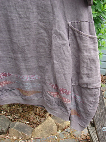 The Barclay Linen Crossover Urchin Dress Feather Border Pebble Size 0 features a V-neckline, drop shoulders, empire waist, curved hem, and double side pockets, embodying vintage Blue Fish Clothing's creative elegance.