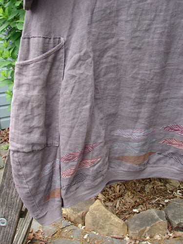 The Barclay Linen Crossover Urchin Dress Feather Border Pebble Size 0 features a V-neckline, drop shoulders, empire waist, curved hem, and double side pockets, embodying vintage Blue Fish Clothing's creative elegance.