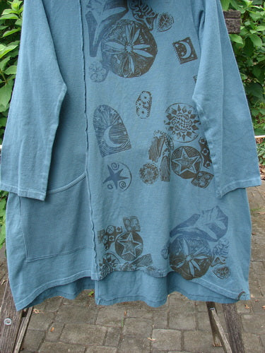 Close-up of the Barclay NWT Eco Cotton Cowl Pocket Tunic Star Moon Hypnea Teal Size 0, featuring a stylish pattern. Visible against a brick surface, this piece embodies the creative spirit of Blue Fish Clothing.