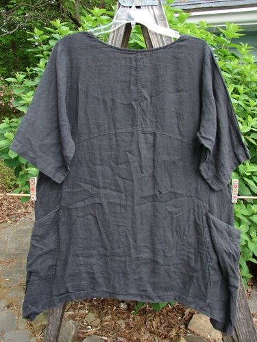 Barclay Linen Two Pocket Urchin Dress features a rounded neckline, sectional panels, and a downward curved empire waist seam. Adorned with a falling branch theme, it includes double drop front wrap pockets.