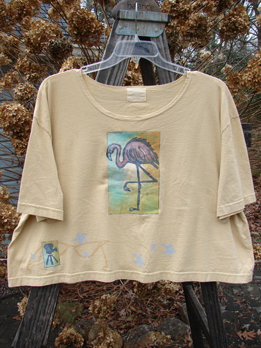 2000 Short Sleeved Crop Tee Flamingo Plantain Size 2 displayed on a wooden hanger, showcasing its wide swingy shape, softly rolled neckline, and signature Blue Fish patch.