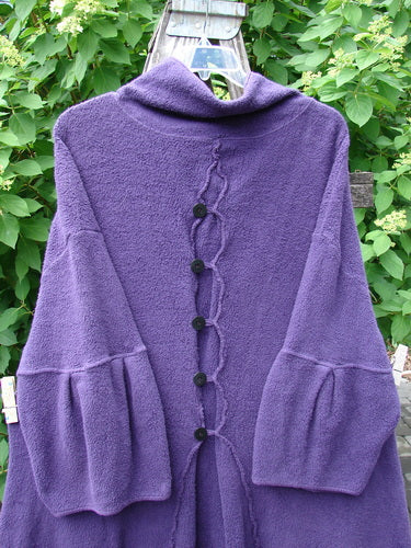 Barclay Patched Celtic Moss Double Snap Button Back Coat Violet OSFA features a deep-purple fleece-like fabric with braided trim, bell sleeves, black button row, and a loose, rounded collar against green foliage.