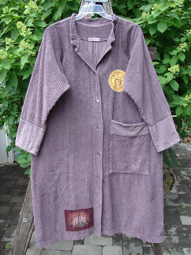 Barclay Patched Chenille Straight Coat Aubergine Dust Size 1, a long, loose-fitting coat with button-front, patch pockets, and decorative fabric patches, crafted from organic cotton chenille, displayed outdoors on a hanger.