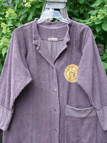 Barclay Patched Chenille Straight Coat in Aubergine Dust, hanging outdoors, showcases button-front corduroy, gold emblem, patch pocket, and long sleeves with rollable canvas lowers, reflecting Blue Fish Clothing's vintage style.