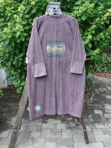 Barclay Patched Chenille Straight Coat in Aubergine Dust hangs on a wooden ladder, featuring long sleeves, wide cuffs, and colorful patches. The coat's stand-up collar and unique patchwork reflect Bluefishfinder.com's vintage style.