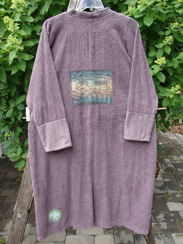 Barclay Patched Chenille Straight Coat Aubergine Dust Size 1, featuring a stylized steam locomotive patch on the back, cozy sleeves with rollable canvas lowers, and metal buttons, displayed outdoors.