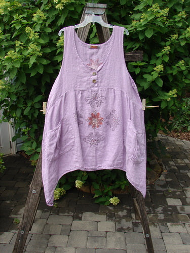 Barclay Linen Tuesday's Pocket Prairie Dress Celtic Floral Lilac Size 1 features a scoop neckline with shell-like buttons, floral embroidery, pleated empire waist, and diagonal patch pockets, draped on a wooden stand.