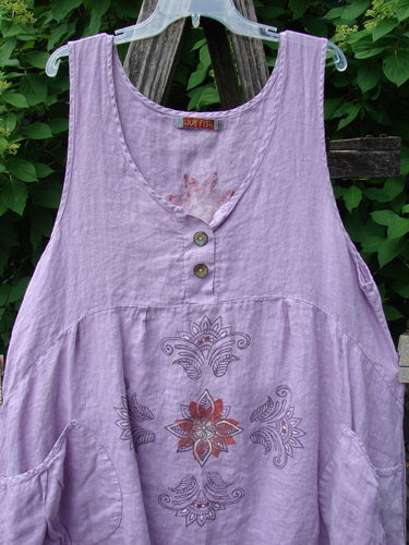 Barclay Linen Tuesday's Pocket Prairie Dress Celtic Floral Lilac Size 1: a sleeveless tunic with scoop neckline, floral pattern, side pockets, and shell buttons, displayed against wooden slats and greenery.