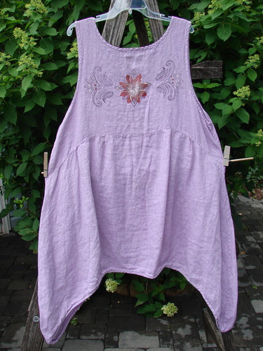 Barclay Linen Tuesday's Pocket Prairie Dress Celtic Floral Lilac Size 1 features a loose, sleeveless design with an embroidered floral motif on the chest, scoop neckline, and asymmetrical hem, hanging outdoors.