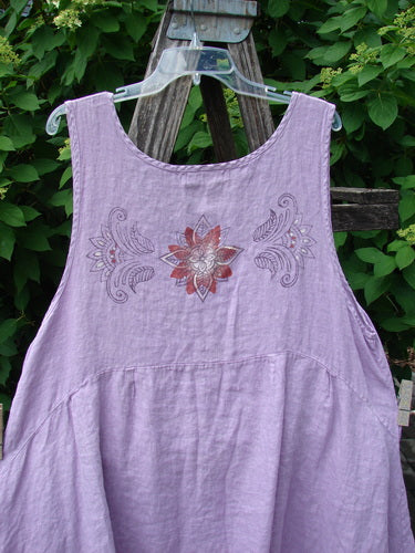 Barclay Linen Tuesday's Pocket Prairie Dress Celtic Floral Lilac Size 1, featuring a scooped neckline, gathered skirt, central mandala embroidery, and diagonal pleated pockets, draped over a garden ladder.