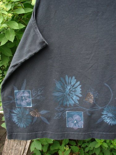 Barclay Cotton Lycra Tank Border Garden Black Size 2, featuring a decorative border of blue flowers and vines, displayed on a wooden bench, with a corner folded to reveal the fabric's underside.