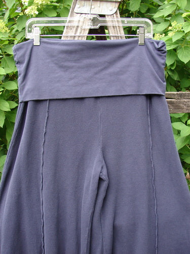 The Barclay Thermal Fold Over Crop Pant Unpainted Deep Violet Size 1 features a relaxed fit with flared legs and vertical seams, elegantly displayed on a hanger against a natural outdoor backdrop.